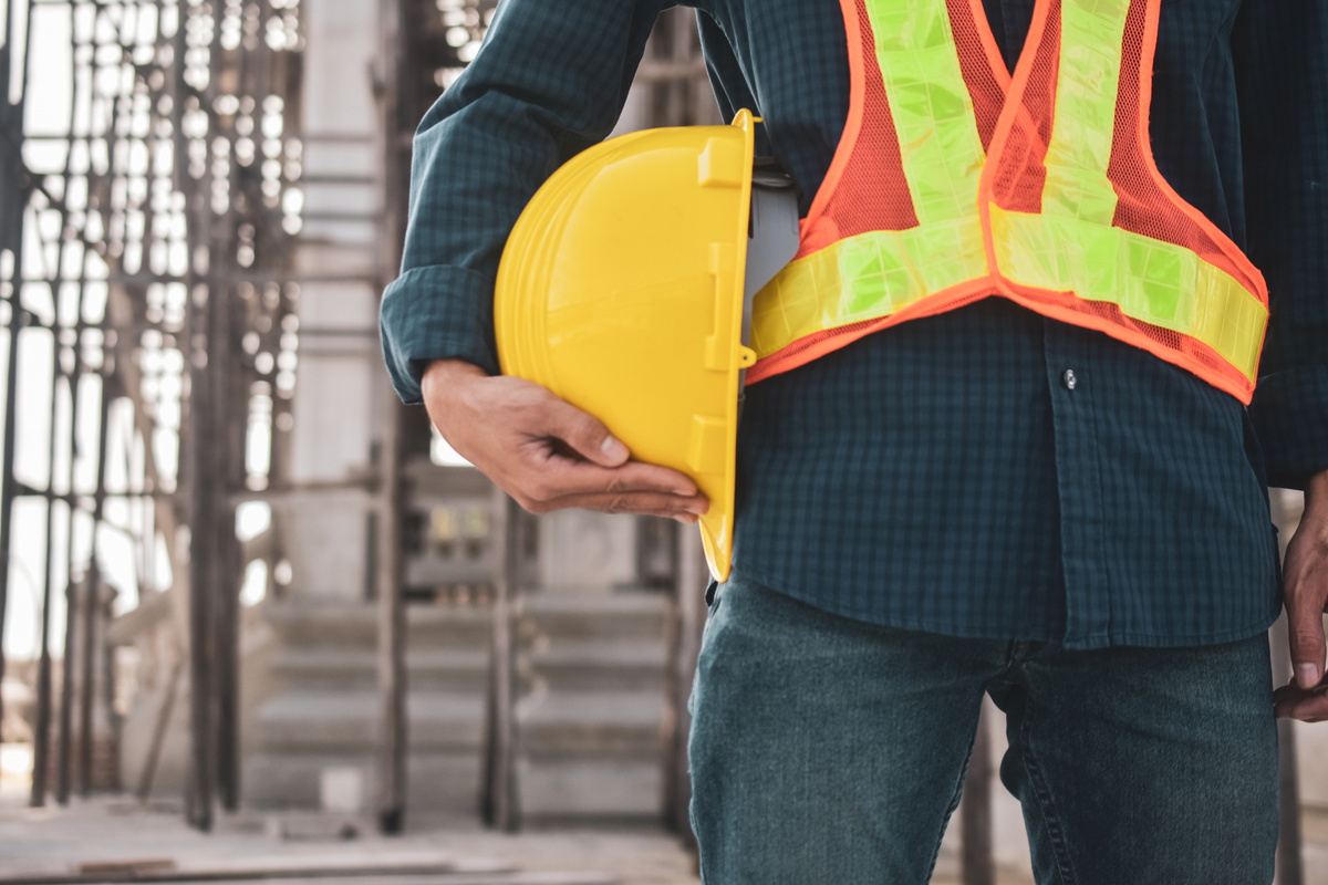 Worker Holding Hard Hat on Construction Site Background